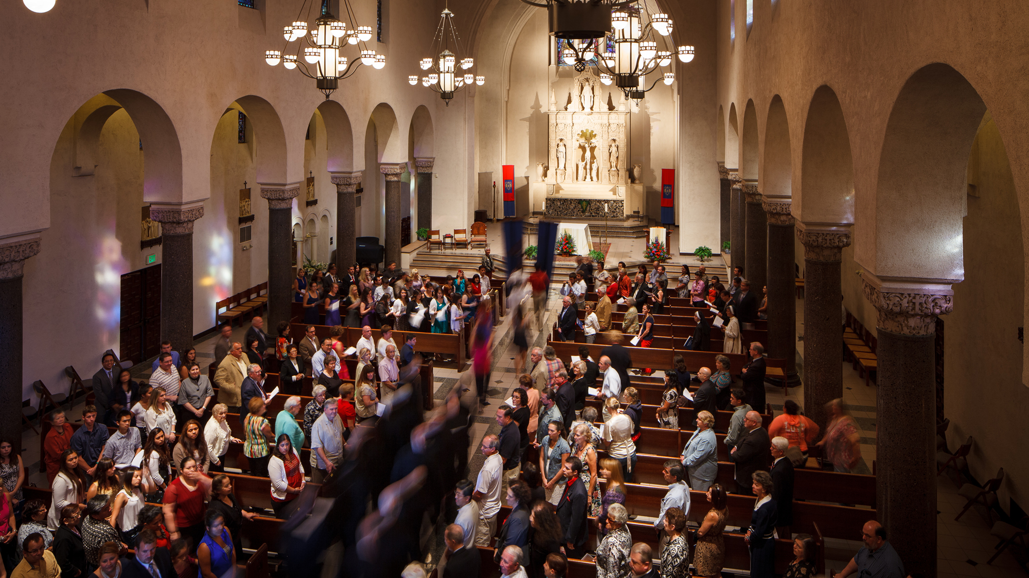 A procession moving down the aisle of the chapel with people in the pews standing up and watching