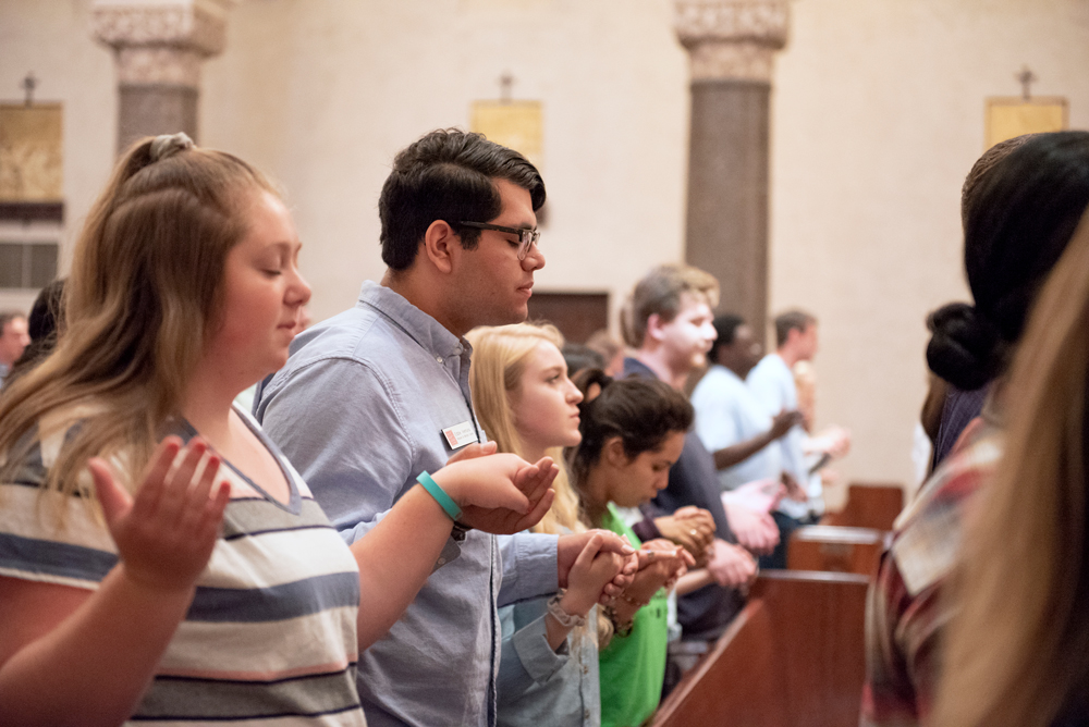 Students standing in the pews of the chapel holding hands with their eyes closed