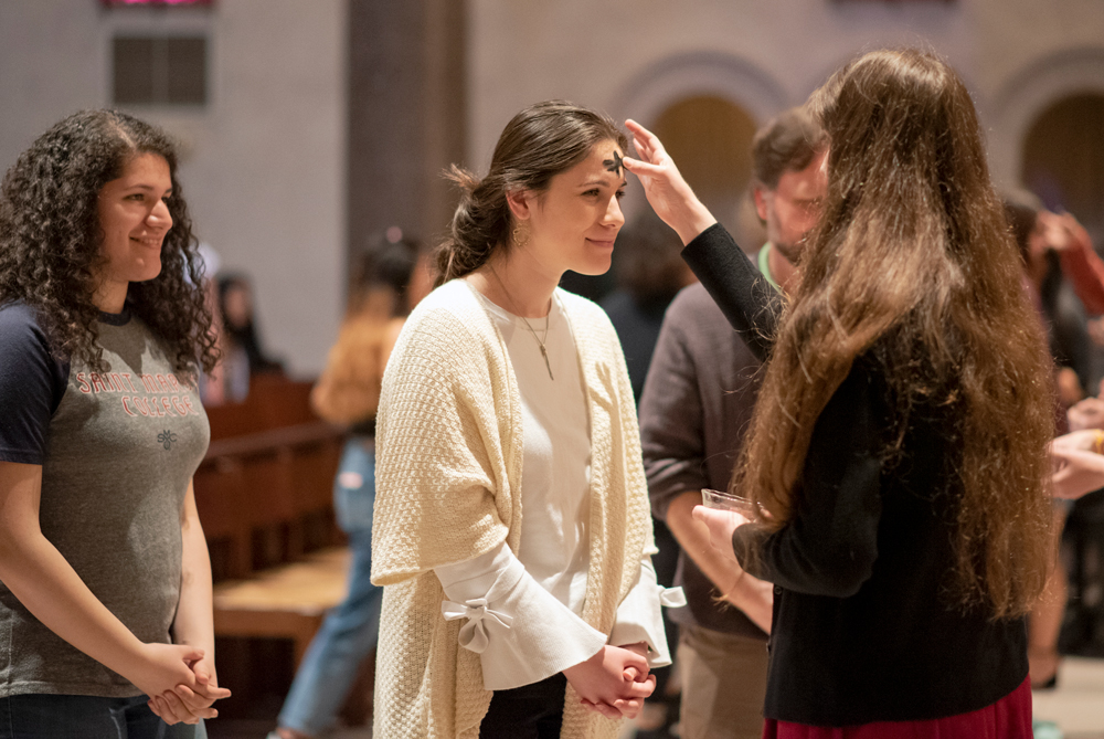 A girl standing in line smiling with her hands folded while a cross is made for Good Friday on her forehead