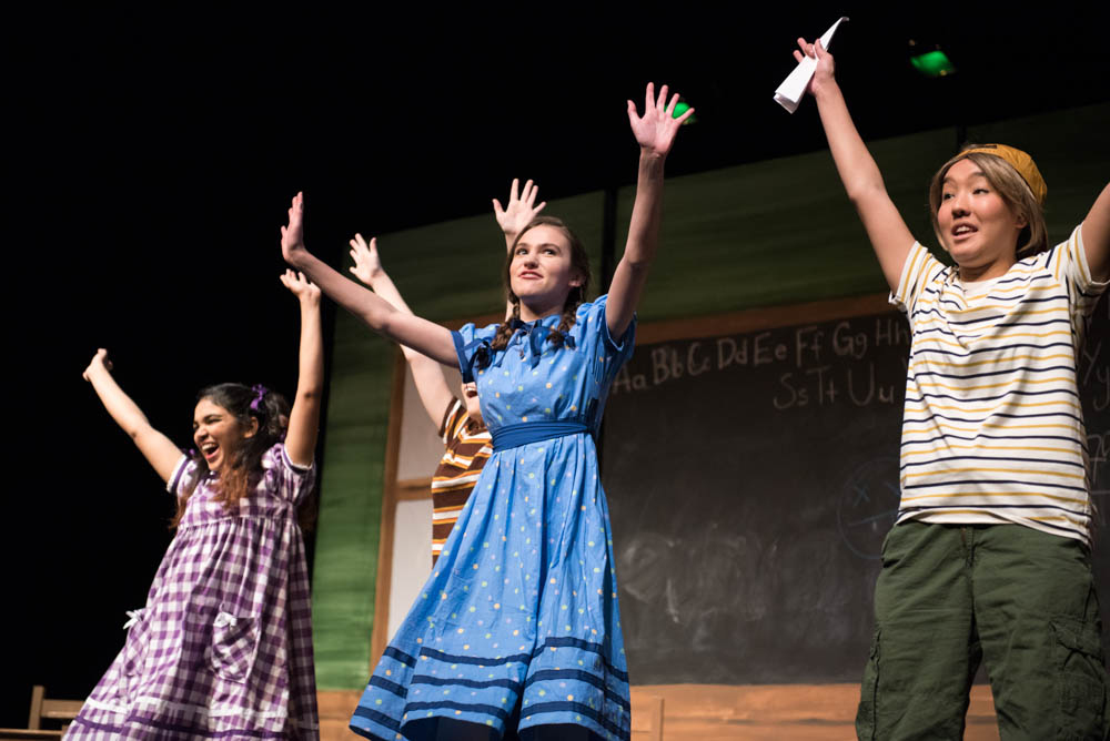 Students with their hands up smiling at the end of a performance of Miss Nelson