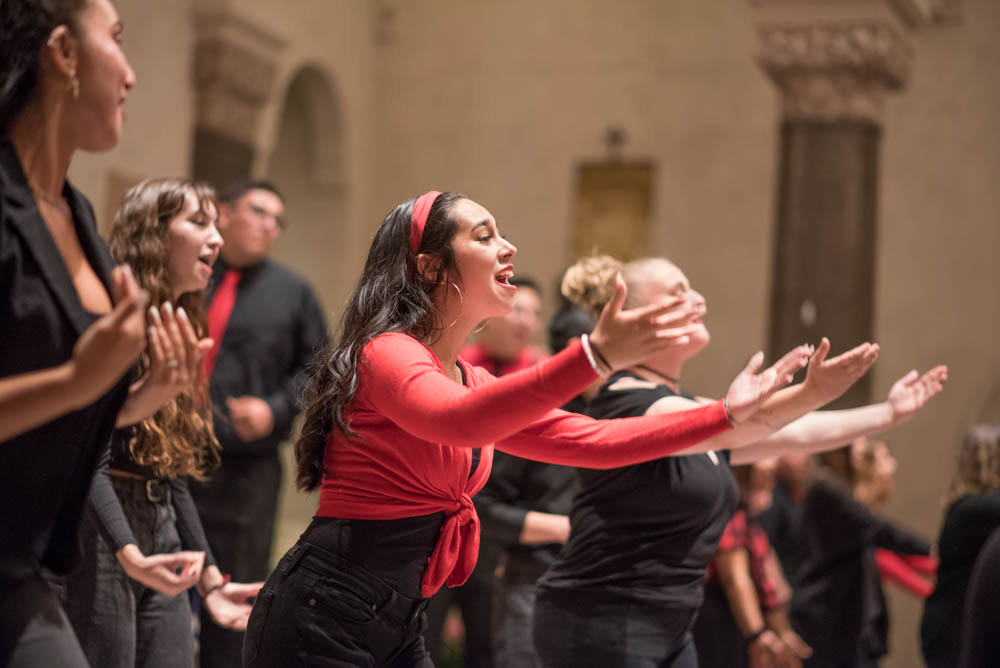 A girl leaning forward with her arms out singing during a choir performance in the chapel