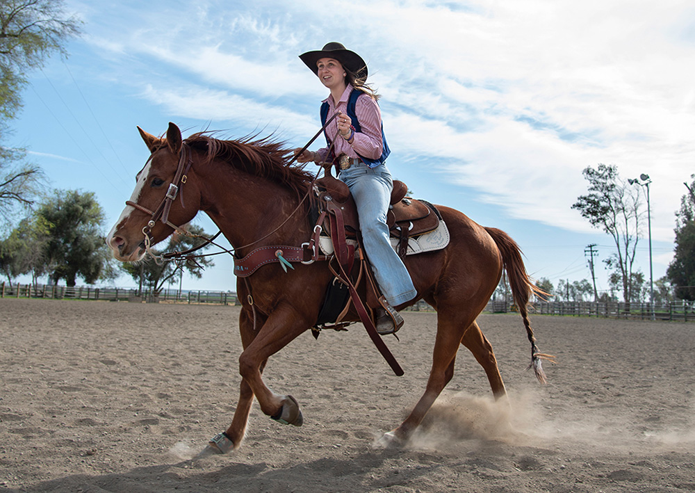 A girl smiling ahead while on the back of a horse that is running