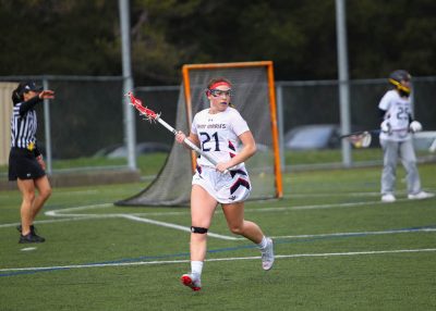 A girl running with a lacrosse stick in front of a goal post