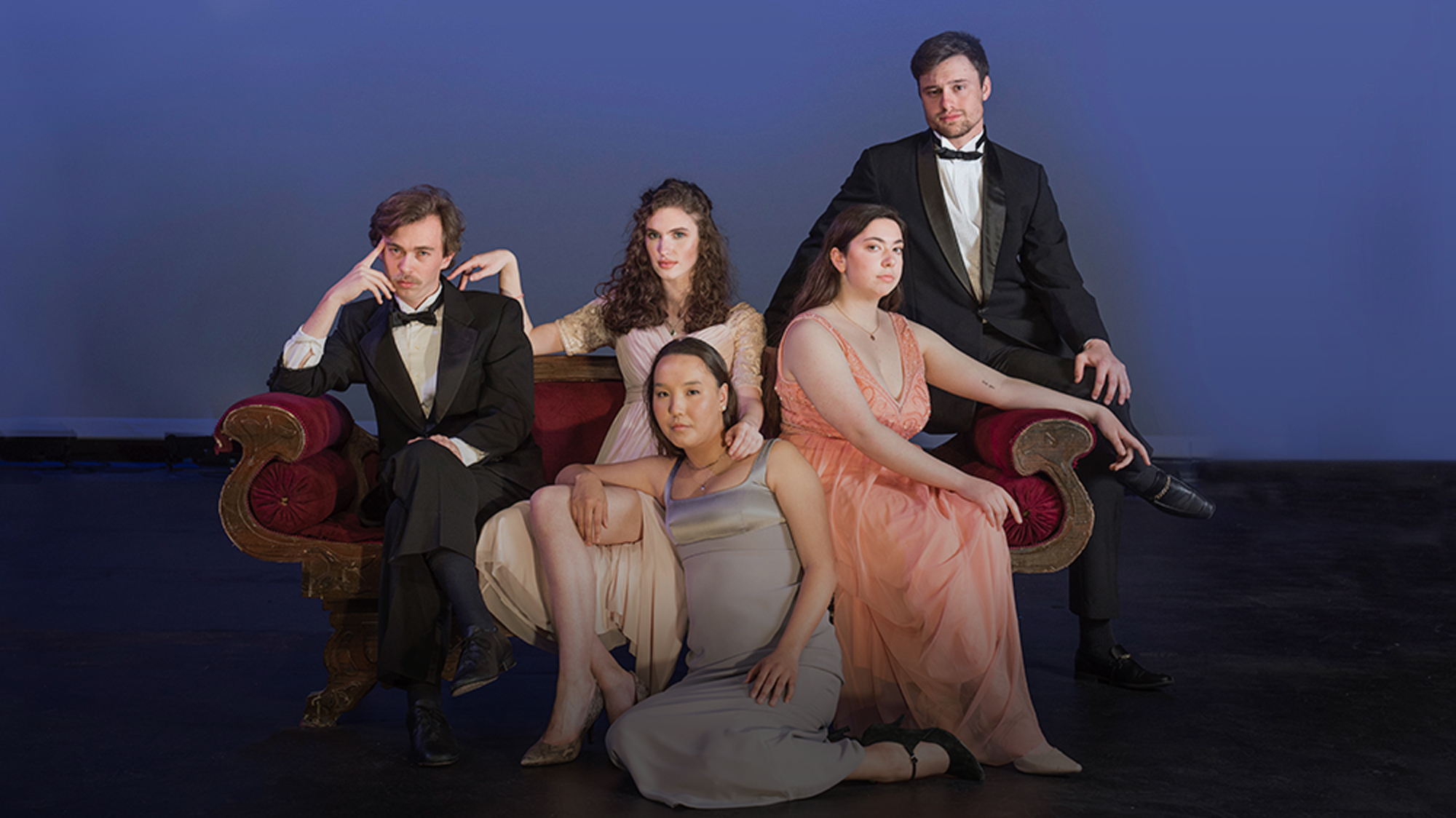 Students wearing black tie clothing while posed on a couch on the stage of LeFevre Theatre