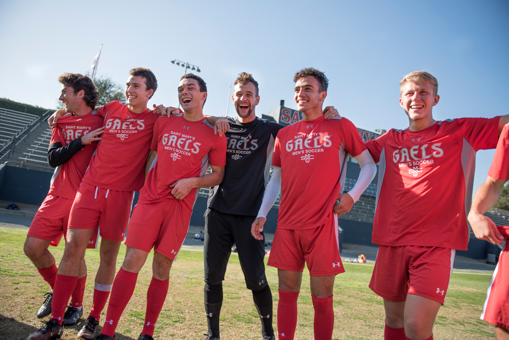 Male soccer players in red jerseys standing in a line laughing with their arms around each other