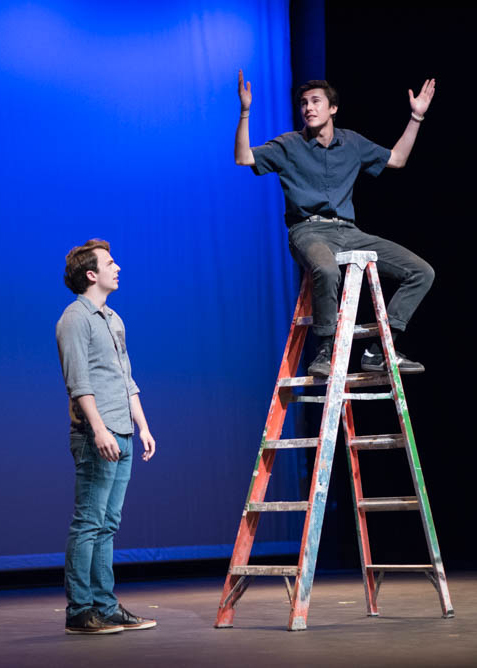 Actor sitting on a ladder with his arms up and another actor looking at him from below while on stage