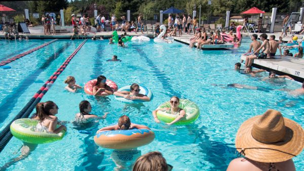 A big pool party with many students in round pool floatys and sitting around the pool