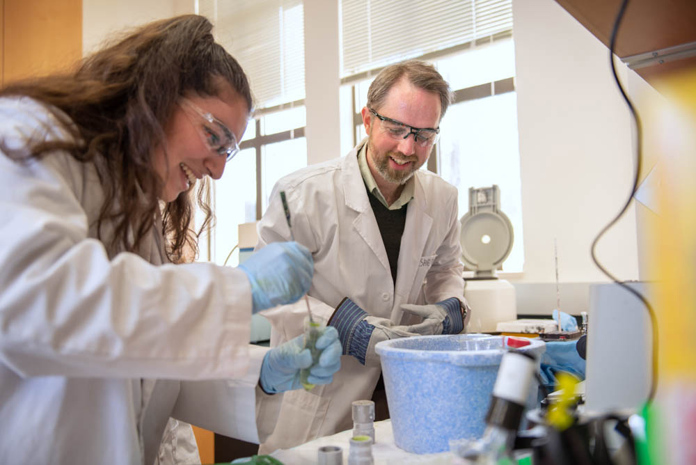 Student and professor smiling in a laboratory while mixing substances