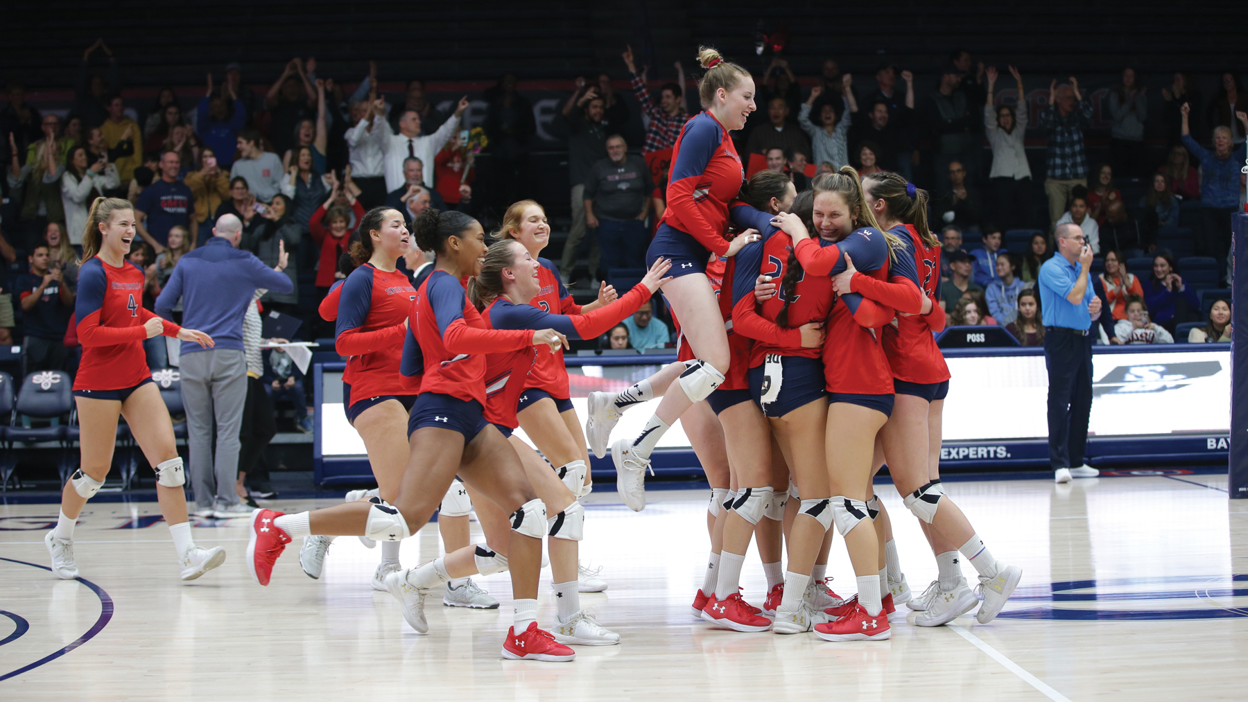 Female Volleyball players jumping up and down with smiles on their face on the floor of UCU Pavilion